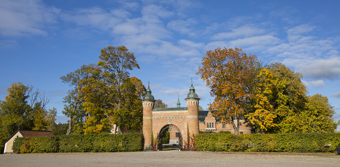 Slottsportal i tegel med stor häck. slott i bakgrunden